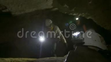 手持手电筒的头盔在洞穴学家面前探索黑暗狭窄的洞穴